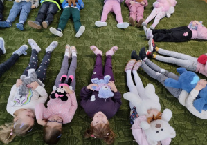 Dzieci leżą na dywanie przytulając misie