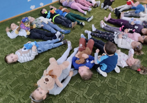 Dzieci leżą na dywanie przytulając misie