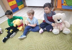 Dzieci siedzą na dywanie z misiami