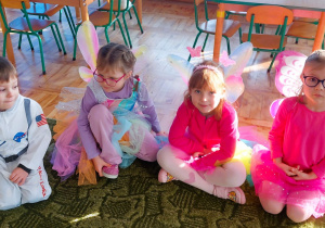 Dzieci siedzą na dywanie w sali przedszkolnej