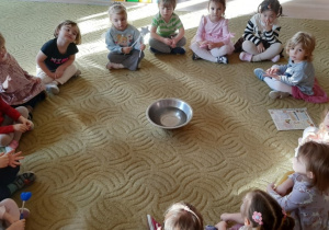 Dzieci siedzą w kole na dywanie w sali