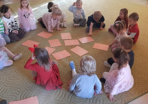 Dzieci siedzą w kole na dywanie w sali czekając na wróżbę