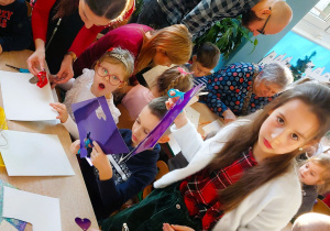 Rodzice z dziećmi wycinają z papieru elementy łańcucha choinkowego