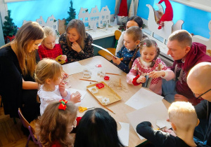 Rodzice z dziećmi wycinają z papieru elementy łańcucha choinkowego