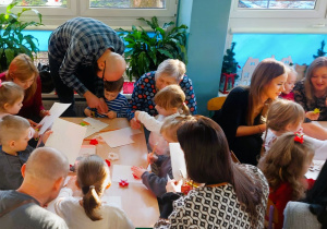 Rodzice z dziećmi wycinają z papieru elementy łańcucha choinkowego