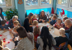 Rodzice z dziećmi wycinają z papieru elementy łańcucha choinkowego