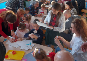 Rodzice z dziećmi wycinają z papieru elementy łańcucha choinkowego