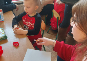 Rodzice z dziećmi wycinają z papieru elementy łańcucha choinkowego