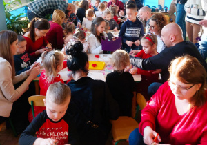 Rodzice z dziećmi wycinają z papieru elementy łańcucha choinkowego