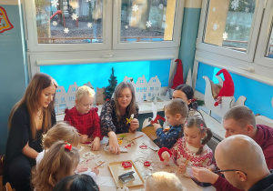 Rodzice z dziećmi wycinają z papieru elementy łańcucha choinkowego