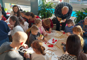 Rodzice z dziećmi wycinają z papieru elementy łańcucha choinkowego