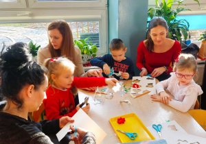 Rodzice z dziećmi wycinają z papieru elementy łańcucha choinkowego