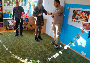 Rodzice trzymają stworzony wraz z dziećmi łańcuch choinkowy