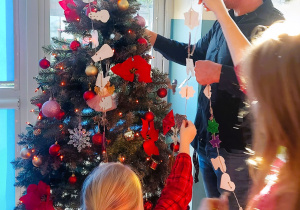 Rodzice z dziećmi ubierają choinkę w stworzone ozdoby choinkowe