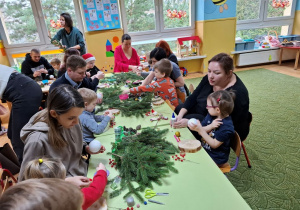 Rodzice z dziećmi tworzą świąteczne stroiki