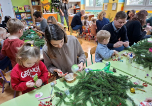 Rodzice z dziećmi tworzą świąteczne stroiki