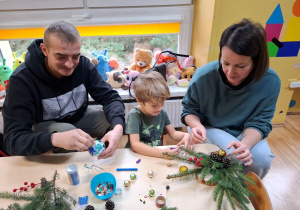 Rodzice z dziećmi tworzą świąteczne stroiki