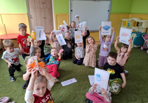 Dzieci siedzą na dywanie trzymając ilustracje dotyczące czystości