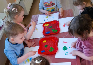 Dzieci malują na kartce palcami zanurzonymi w kolorowych farbach