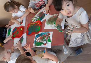 Dzieci malują na kartce palcami zanurzonymi w kolorowych farbach