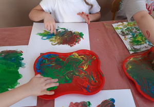 Dzieci malują na kartce palcami zanurzonymi w kolorowych farbach