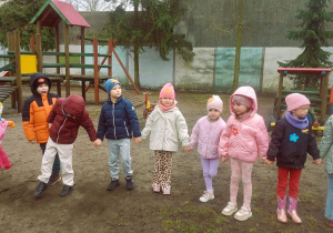 Dzieci stoją ustawione w kole w ogrodzie przedszkolnym