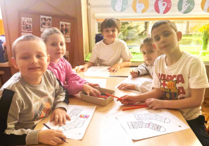 Dzieci siedzą przy stolikach i kolorują