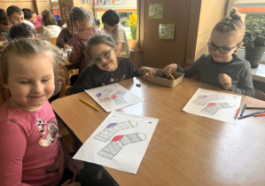 Dzieci siedzą przy stolikach i kolorują