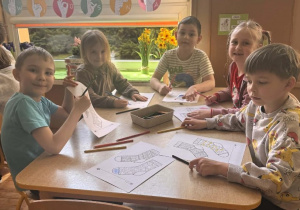 Dzieci siedzą przy stolikach i kolorują