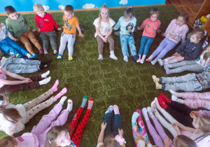 Dzieci siedzą w kole pokazując kolorowe skarpetki na swoich stopach