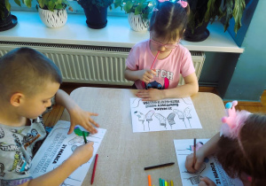 Dzieci siedzą przy stolikach i kolorują