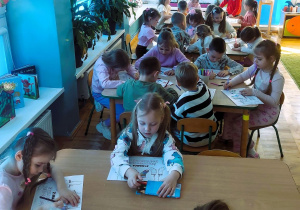 Dzieci siedzą przy stolikach i kolorują