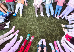 Dzieci siedzą w kole pokazując kolorowe skarpetki na swoich stopach