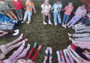 Dzieci siedzą w kole pokazując kolorowe skarpetki na swoich stopach