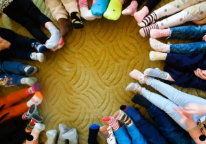 Dzieci siedzą w kole pokazując kolorowe skarpetki na swoich stopach