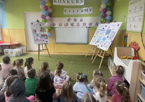 Dzieci siedzą na dywanie czekając na ogłoszenie wyników konkursu plastycznego na podstawie serii opowiadań "Pan Kuleczka"