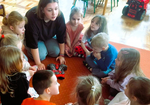 Dzieci siedzą na dywanie w kole obserwując zabawkowe narzędzia do naprawy aut