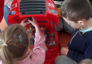 Dziewczynka wkręca plastikową śrubę pod maską zabawkowego samochodu