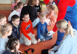 Dzieci w zespołach siedzą na dywanie konstruując z części poszczególne pojazdy