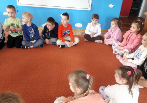 Dzieci siedzą w sali przedszkolnej na dywanie