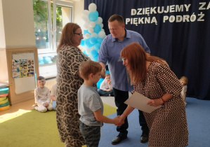 Chłopiec odbiera dyplom od dyrekcji i wychowawcę