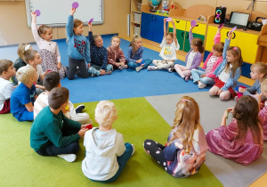 Dzieci siedzą na dywanie trzymając kolorowe kropki