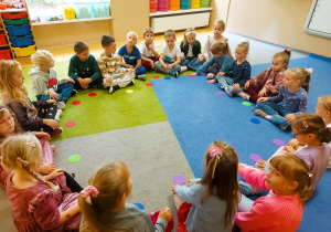 Dzieci siedzą na dywanie trzymając kolorowe kropki