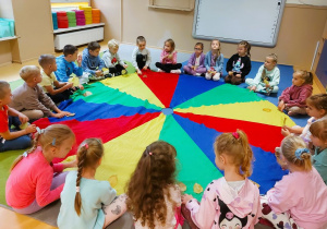 Dzieci siedzą w kole trzymając w rękach liście