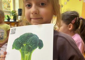 Dziewczynka pokazuje ilustrację przedstawiającą brokuła