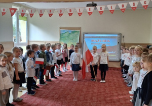 Przedszkolaki w strojach galowych śpiewają hymn, uroczyście obchodząc Narodowe Święto Niepodległości