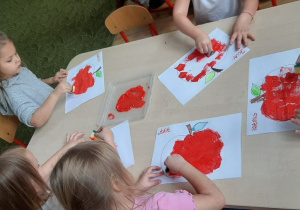 Dzieci stemplują kontur jabłka gąbką z czerwoną farbą