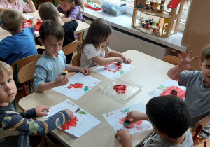 Dzieci stemplują kontur jabłka gąbką z czerwoną farbą