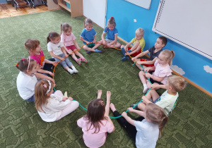 Dzieci siedzą w kole na dywanie w sali przedszkolnej
